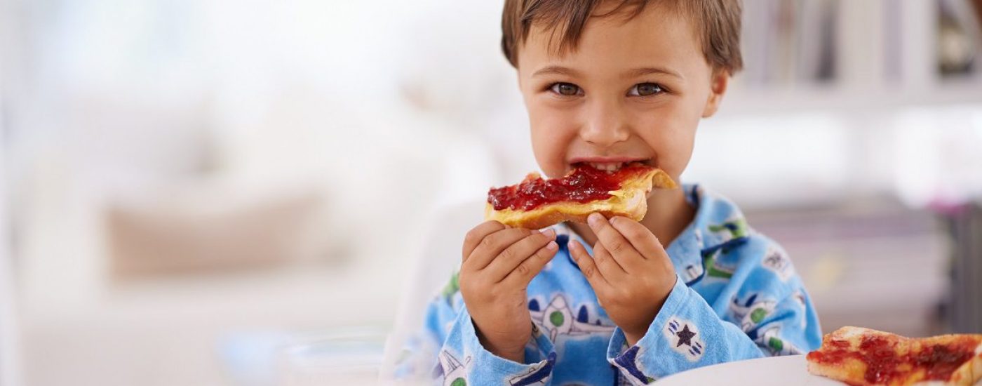A cute little boy eating toast with jam